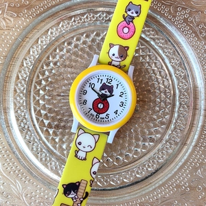 Detail of yellow kids watch with cute cat and donut prints on a glass display plate
