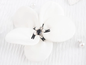 Close-up of a white fabric 3D flower with black gemstone and pearls on a textured blouse