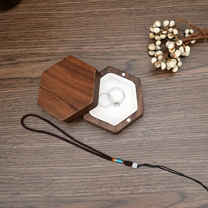 Macro shot of two rings in a hexagonal dark walnut jewelry box with white cushion