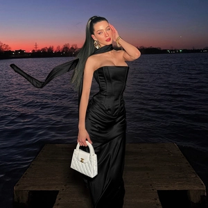 Elegante abito in raso nero con nastro al collo su uno sfondo di tramonto in riva al lago