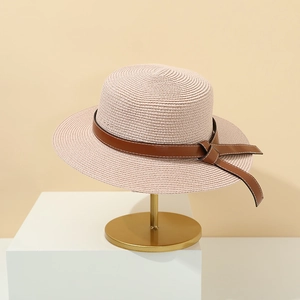 Detail of beige straw sun hat featuring brown leather strap with fine white stitching