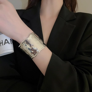 Close-up of a wide silver cuff bracelet with irregular wave texture on a black suit sleeve