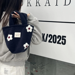 Detail of navy blue plush knit handbag featuring 3D white floral appliqués and logo