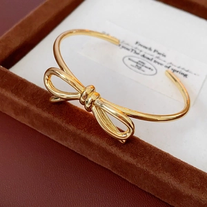 Vista macro di un bracciale rigido a fiocco dorato su un vassoio portaoggetti marrone