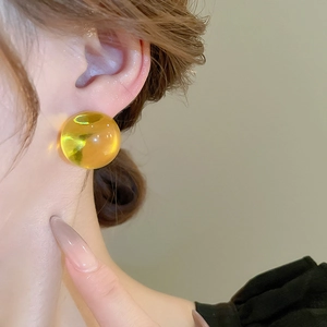 Gros plan d'un modèle portant une boucle d'oreille boule en résine ambre transparente et lisse