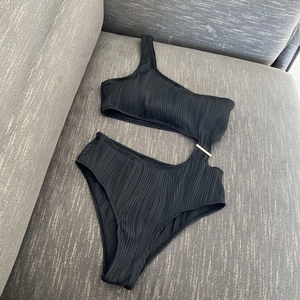 Detail of one-shoulder ribbed swimsuit featuring side cut-outs and a gold metal buckle
