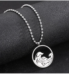 Détail d'un pendentif rond argenté avec gravure de vagues et chaîne à billes sur fond noir