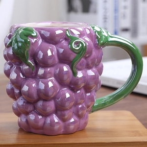 Handcrafted purple grape ceramic mug with green leaf handle on a wooden tray