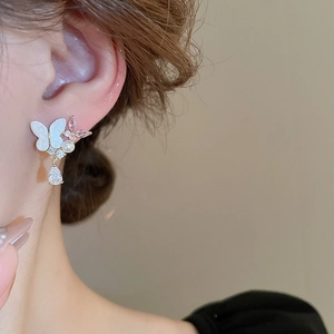 Close-up of butterfly earrings with pearls and pink zircon pendants on a female model
