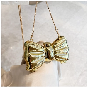 Detail of a shiny gold bow-shaped acrylic evening clutch with a sleek metallic chain strap
