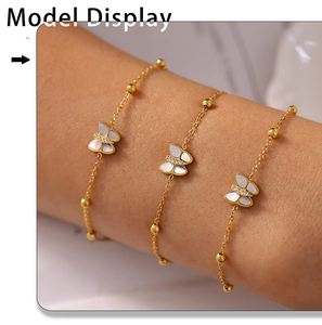 Close-up of a model wearing a gold butterfly bracelet with white mother of pearl and zircons