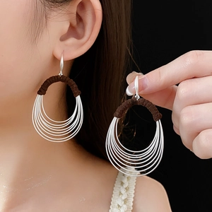 Detailed close-up of oval multilayer silver hoops with brown woven thread accents