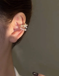 Detailed close-up of a gold-plated flower ear cuff with zircon and pearls on a model