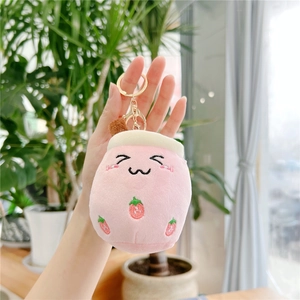 Detailed close-up of a pink plush strawberry keychain with embroidered face and gold clasp