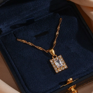 Detailed view of a gold square zircon pendant on a twisted chain inside a blue velvet box