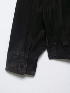 Detail of black suede jacket featuring elastic hem and buttoned cuffs close-up