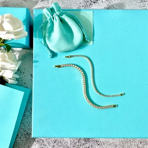 Detailed view of gold tennis bracelets with white and green zircons and gift packaging
