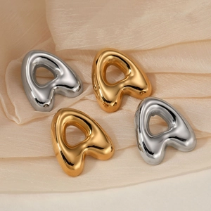 Polished gold and silver stainless steel letter A stud earrings on soft beige fabric