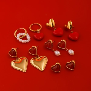 Flat lay of multiple gold stainless steel heart earrings with red resin and pearl details