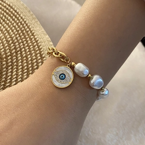 Detailed view of evil eye pearl bracelet with gold chain on model wearing straw hat