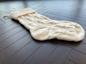 White cable knit Christmas stocking with hanging loop on dark wood floor detail