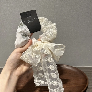 Detail of white lace floral embroidery scrunchie with long ribbon bow and brand tag