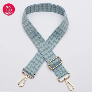 Close-up of wide woven houndstooth bag strap with adjustable gold buckle and spring clips