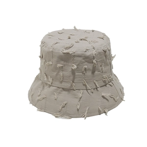 Detail of beige cotton bucket hat featuring unique frayed edges and tassel texture