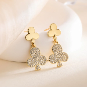 Elegant gold club-shaped drop earrings with pavé-set white zircon on a soft beige surface