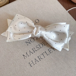 Detailed close-up of a satin polka dot bow hair clip showing refined fabric texture