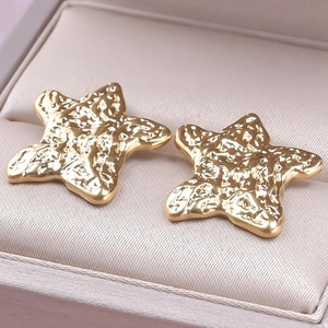 Macro shot of gold star studs with hammer textured finish in a beige jewelry box