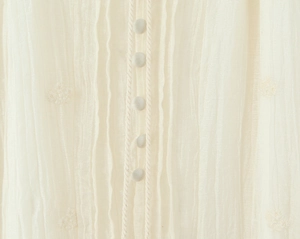 Détail de robe crème avec broderie florale et boutons recouverts de tissu fin