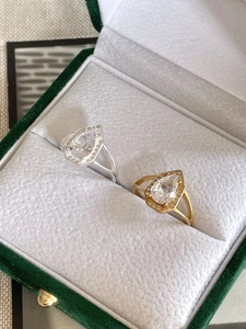 Close-up of pear-cut silver and gold rings with micro-pave halo in a green velvet box