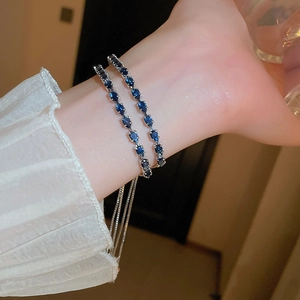 Close-up of a silver double-chain bracelet featuring blue pear-cut stones on a wrist