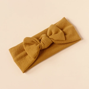 Detailed knit texture of mustard yellow baby headband with decorative bow on beige surface