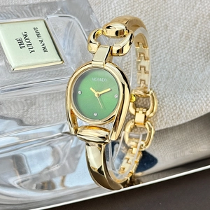 Close-up of golden horseshoe case watch with green dial and diamonds on silk background