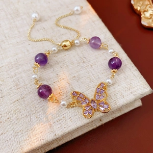 Detail of amethyst and pearl bracelet with a gold butterfly charm on linen background