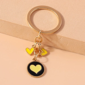 Detail of gold keychain featuring black round pendant with yellow enamel heart charms