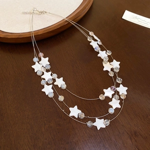 Détail d'un collier à trois couches avec des breloques étoiles blanches et perles claires
