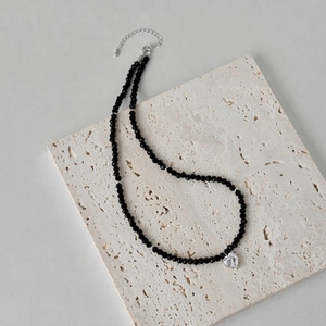 Close-up of black faceted beads necklace with a clear heart pendant on textured stone