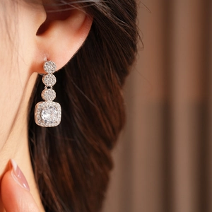 Macro detail of rose gold earrings with square pendants and sparkling cubic zirconia stones