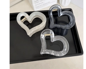Three heart-shaped resin hair claws in cream, grey, and clear colors on a black tray