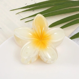 Pearlescent frangipani hair claw clip with yellow gradient center on a summer plate