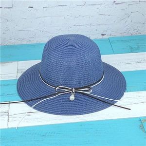 Detail of dark blue straw sun hat featuring a black and white bow with pearl pendant