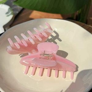 Detail of a large pink jelly-colored hair claw clip with a gold spring on a ceramic plate