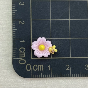 Pink resin flower charm with small yellow bee on grid mat for nail art and jewelry making