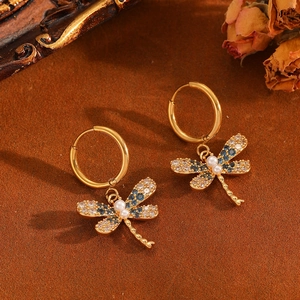 Elegante Libellen-Ohrringe in Gold mit blauen Kristallen und Perlen vor Vintage-Dekor