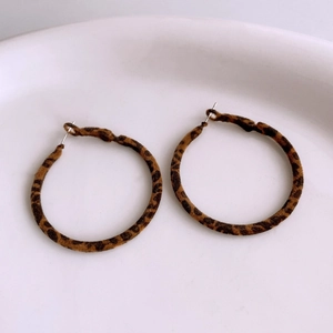Close-up of leopard print hoop earrings in brown and black tones on a white ceramic plate