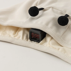 Detail showing safety test of beige knit baby hat with black pom-poms and zero detection result
