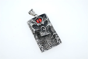 Macro detail of silver skull pendant with red gemstone eye and gothic relief texture